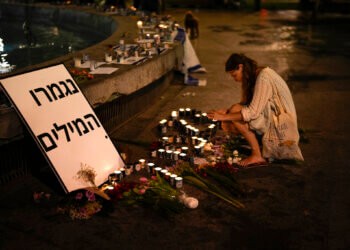 A woman lights candles in honor of victims of the Hamas attacks during a vigil at Dizengoff square in central Tel Aviv, Israel, Friday, Oct. 13, 2023. The sign reads: “Out of Words.” (AP Photo/Francisco Seco)