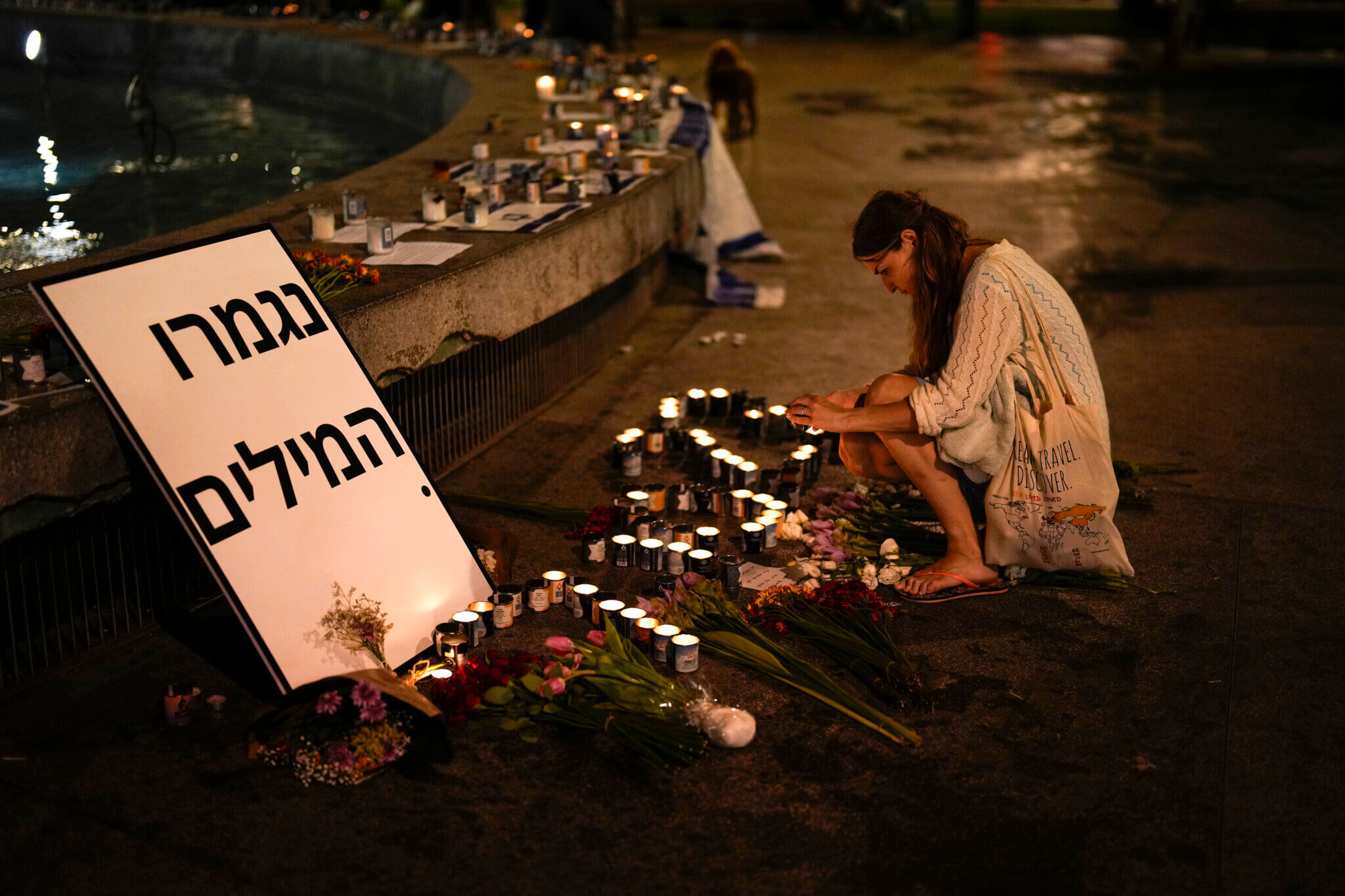 A woman lights candles in honor of victims of the Hamas attacks during a vigil at Dizengoff square in central Tel Aviv, Israel, Friday, Oct. 13, 2023. The sign reads: “Out of Words.” (AP Photo/Francisco Seco)