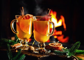 Mulled cider glasses on the background of fireplace fire. Hot mulled spiced apple cider cocktail for winter or autumn time.