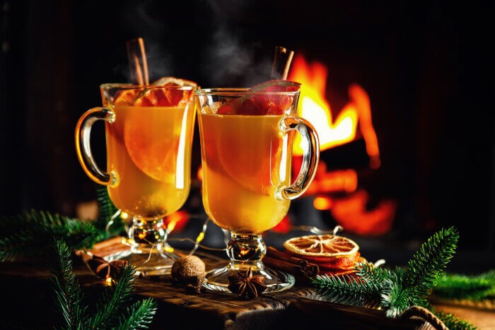 Mulled cider glasses on the background of fireplace fire. Hot mulled spiced apple cider cocktail for winter or autumn time.