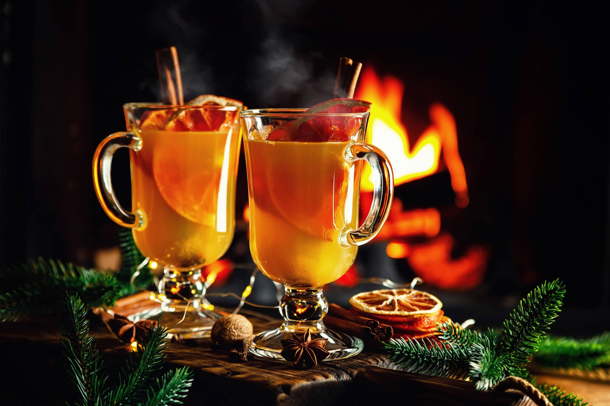Mulled cider glasses on the background of fireplace fire. Hot mulled spiced apple cider cocktail for winter or autumn time.