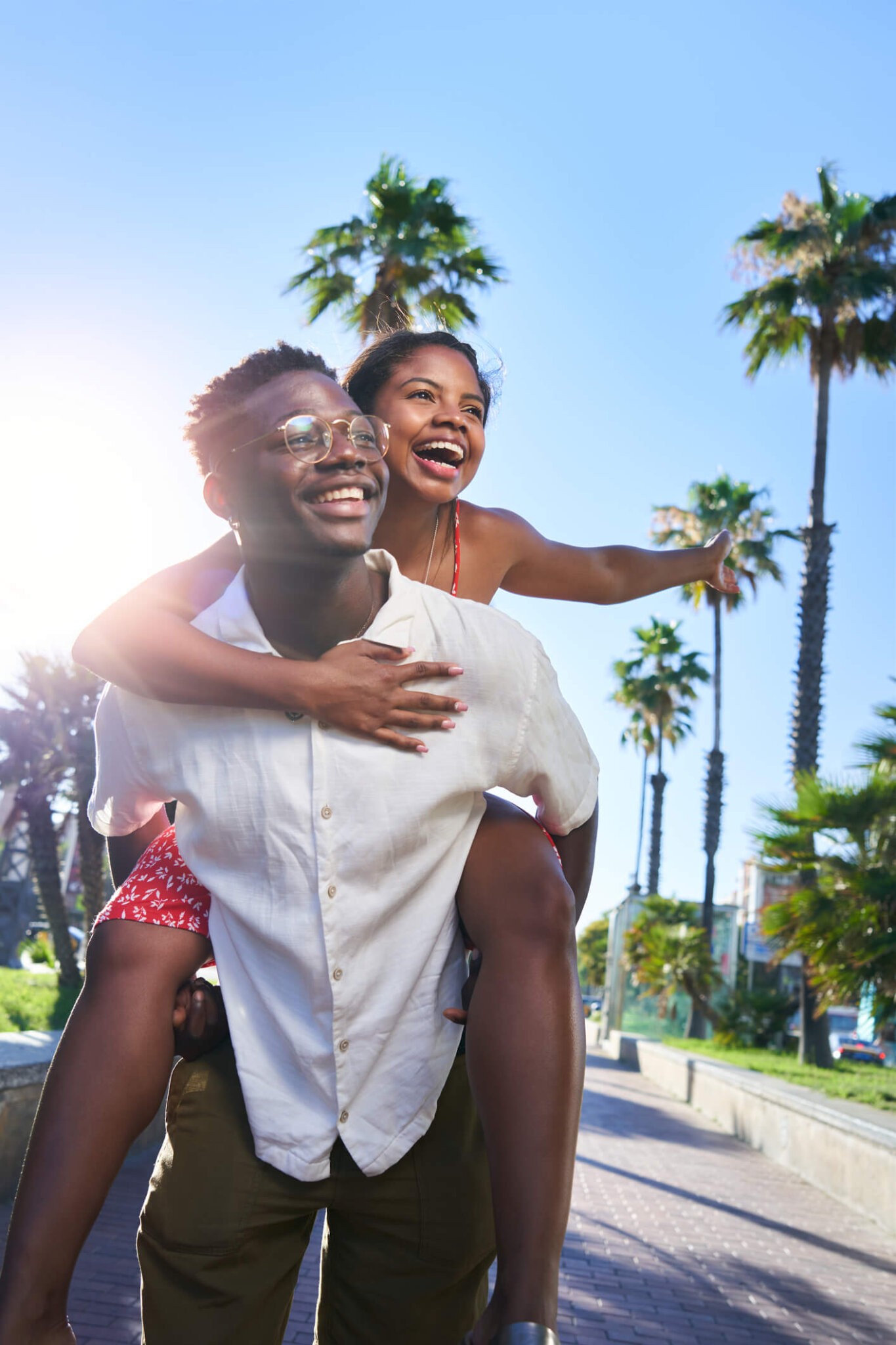 Cheerful portrait of a young mixed race couple on their holidays on an island. African man giving piggyback ride to his Latina girlfriend. Palm trees background . High quality photo