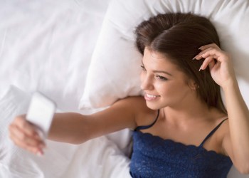 Young attractive brunette makes sexting selfie in bed