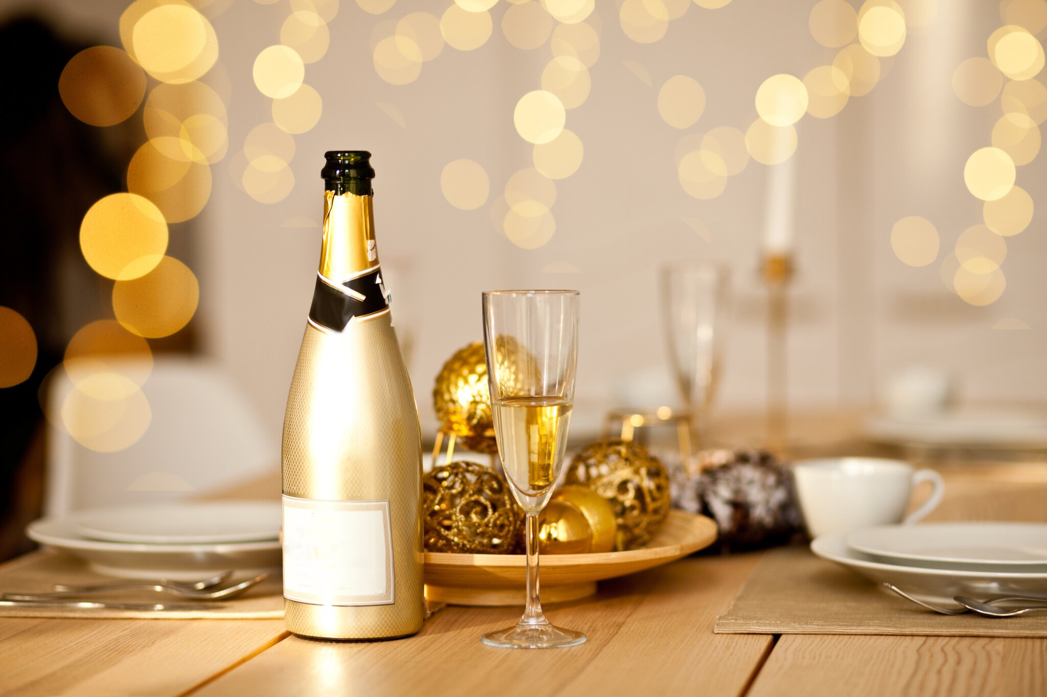 Christmas table setting with holiday decorations in a gold color. New Year celebration. A bottle and glass of champagne