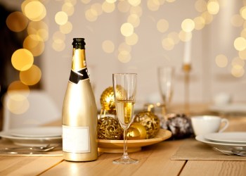 Christmas table setting with holiday decorations in a gold color. New Year celebration. A bottle and glass of champagne