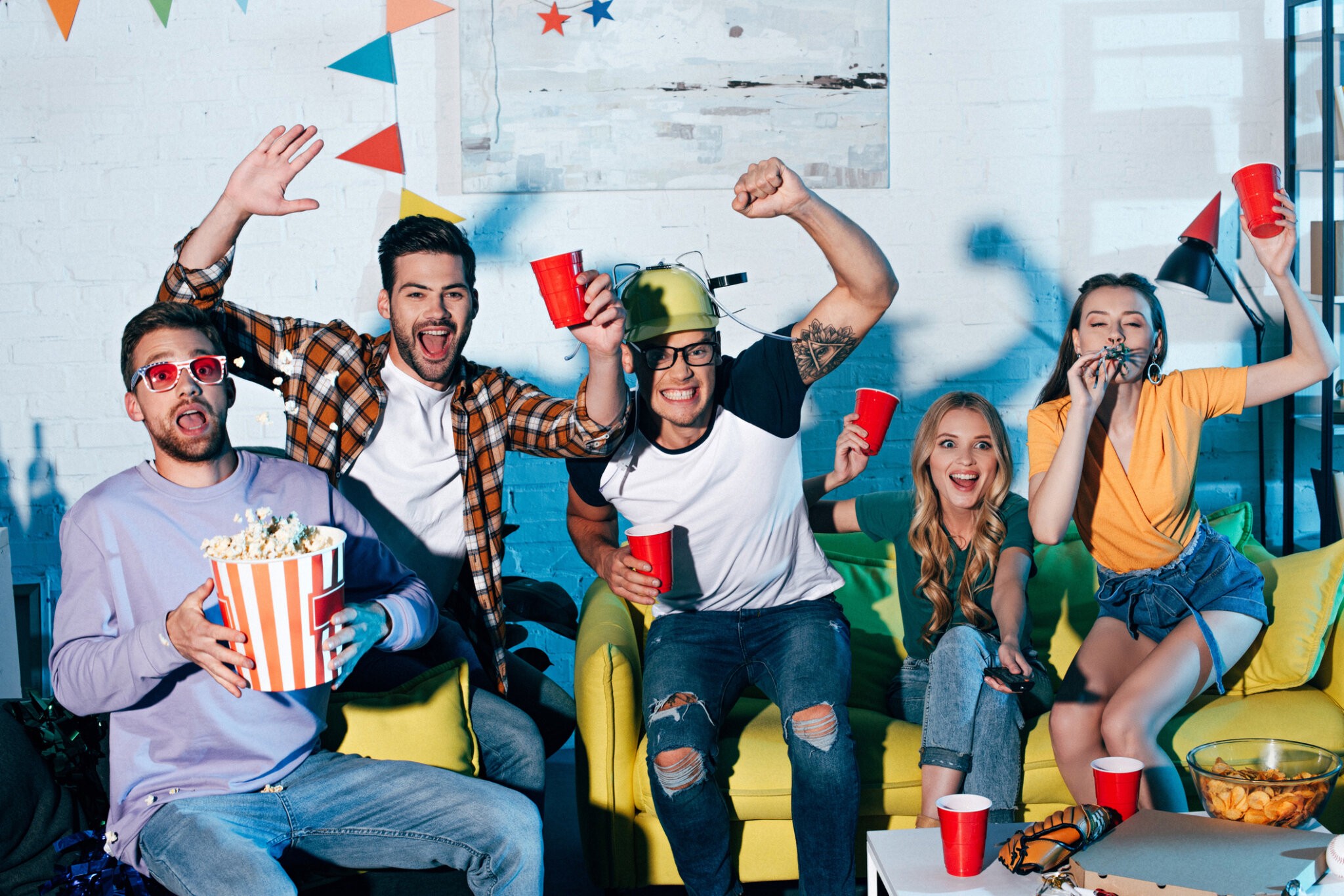 excited young friends drinking beer and eating snacks at home party