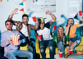 excited young friends drinking beer and eating snacks at home party
