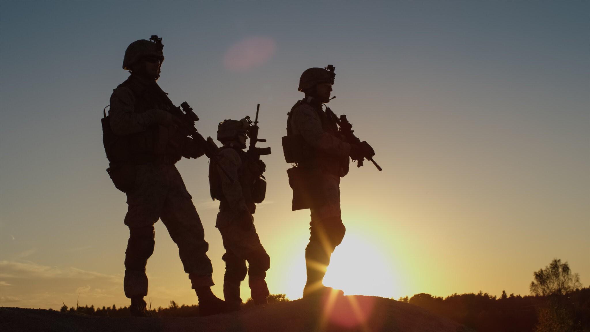 Squad of Three Fully Equipped and Armed Soldiers Standing on Hill in Desert Environment in Sunset Light. War