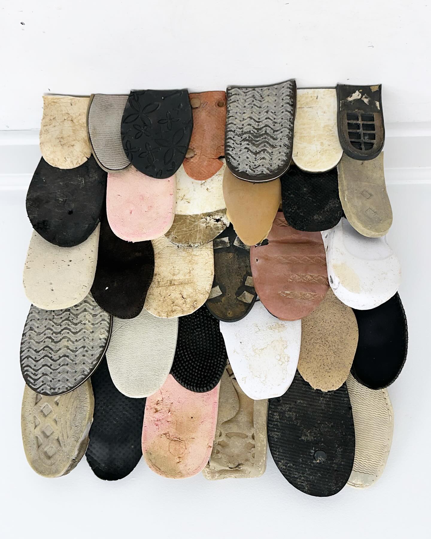 Scott Bluedorn's “Lost Soles V” (2024, found shoe soles on wood, 24” x 24”)
