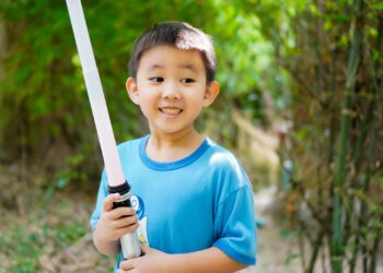 The picture shows a boy smiling happily as he plays a kids lightsaber duel with his brother.