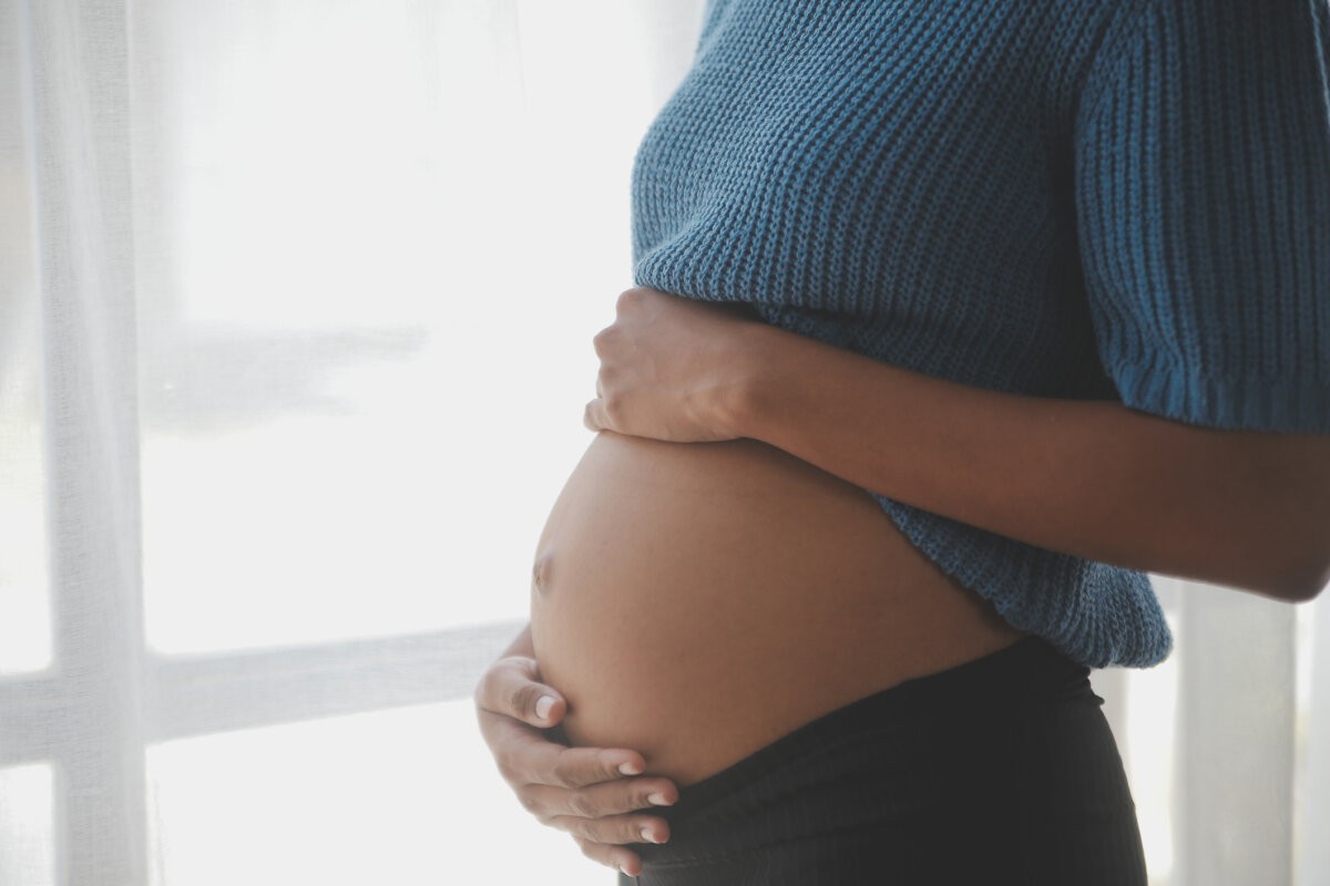 Happy pregnant woman touching belly in front of white wall - Soundview Pregnancy Services helps women make choices