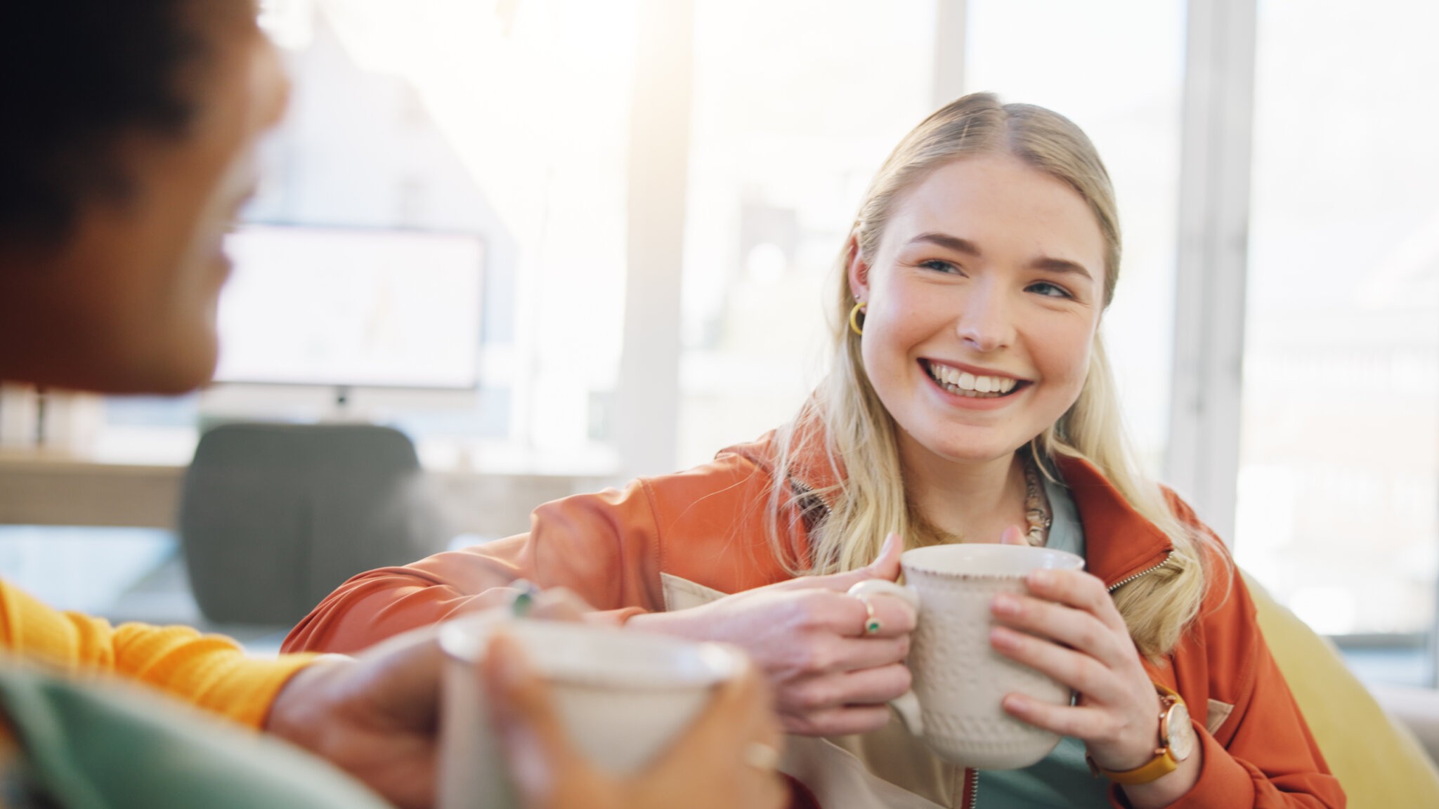 Coffee, friends and women in conversation in home on sofa, bonding or having fun together. Happy, girls talking and tea in lounge, smile and people drink espresso in living room of interracial house happiness