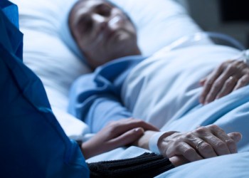 Young woman holding hands and saying goodbye to her dying of cancer mother in hospice on her deathbed