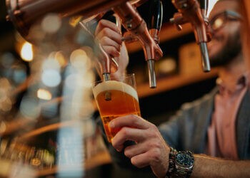 Tattooed caucasian barman pouring beer while standing in pub. Like a nice Hamptons bars pubs or tavern