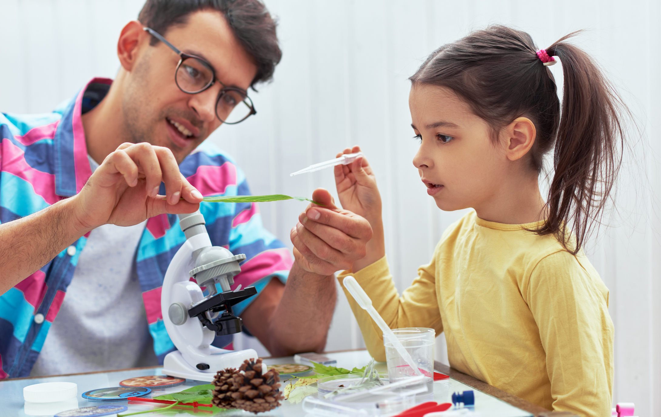 Handsome dad and cute daughter study biology and chemistry lesson with microscope. Little girl with father doing science experiments on the leaf in the laboratory. Homeschooling and education concept.