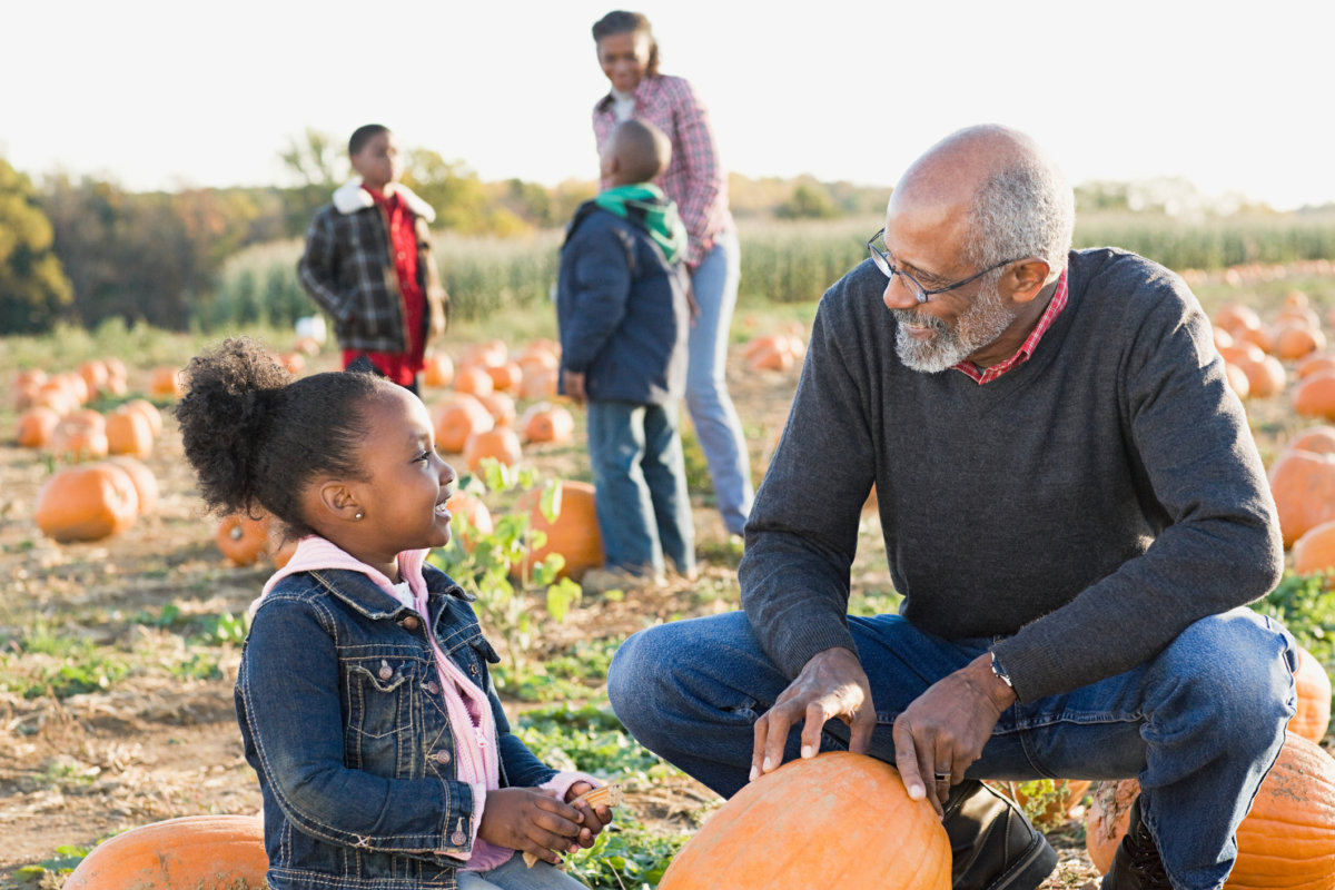 A grandfather and his granddaughter looking at pumpkins while pumpkin picking