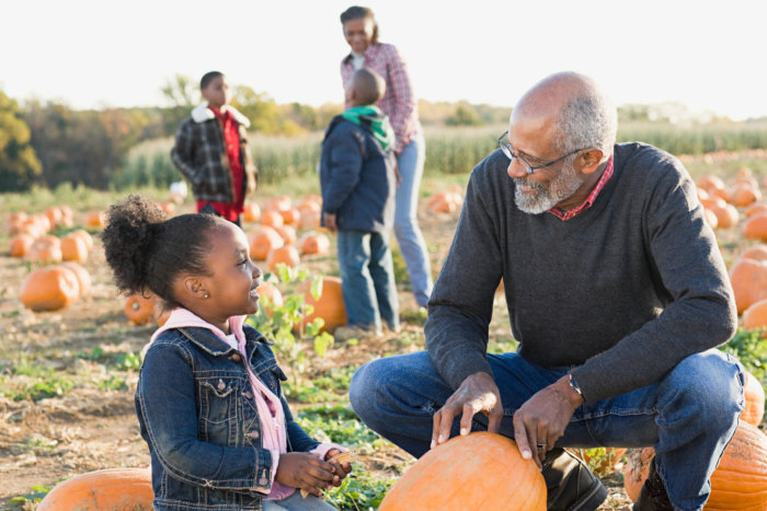 A grandfather and his granddaughter looking at pumpkins while kids are pumpkin picking