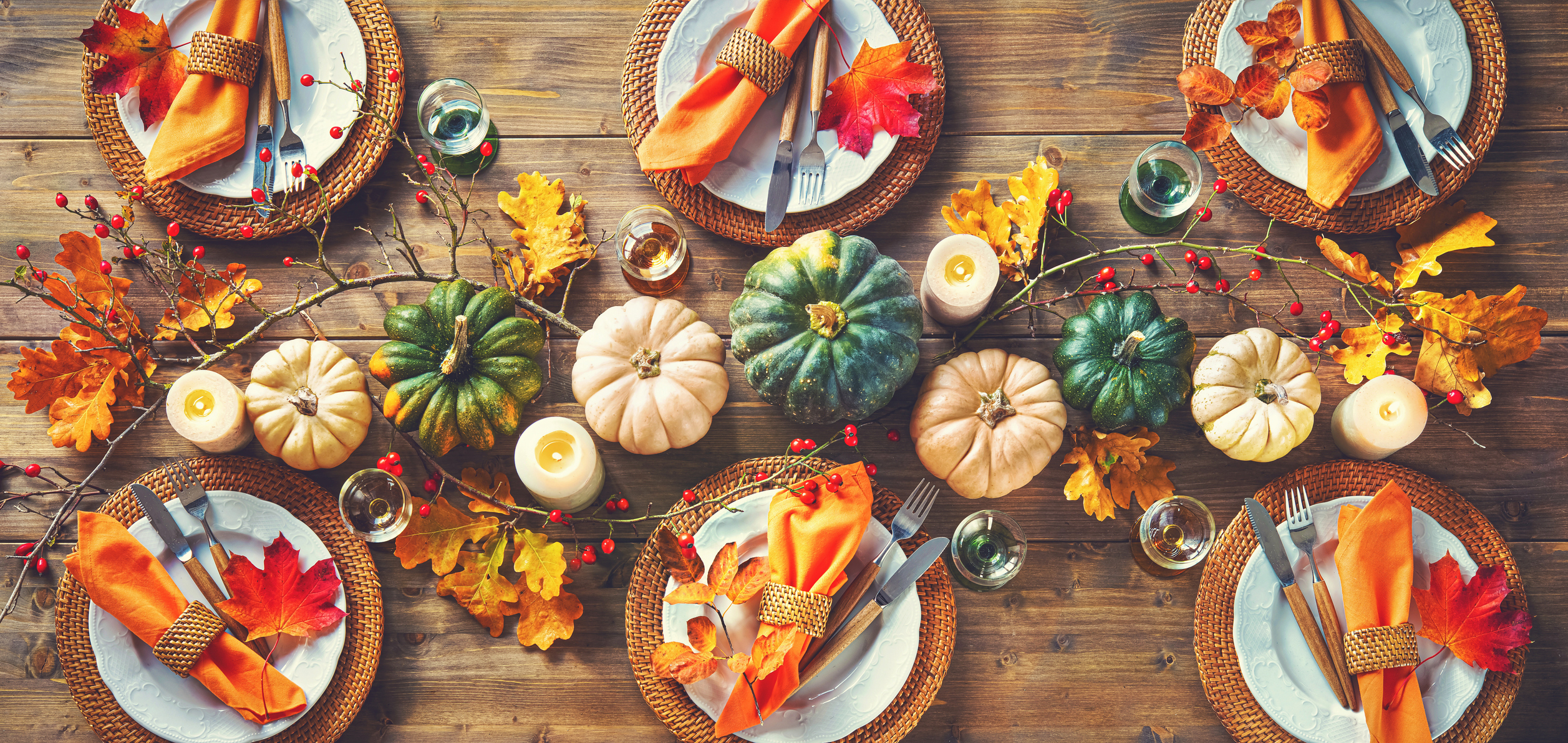 Autumnal decorated table for celebrating Thanksgiving or other family celebration. Festive table setting with plates, glassware, pumpkins, rose hip branches and leaves on wooden table background, top view