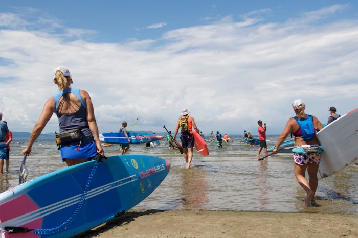Standup paddlers enter the water - like in Stand Up for the Ocean